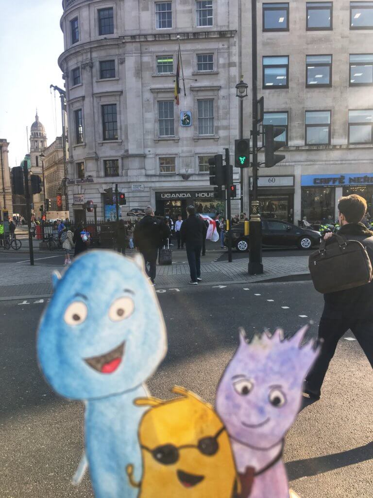 Alex, Valentin*a und Curly vor einer queere Ampel am Trafalgar Square London.